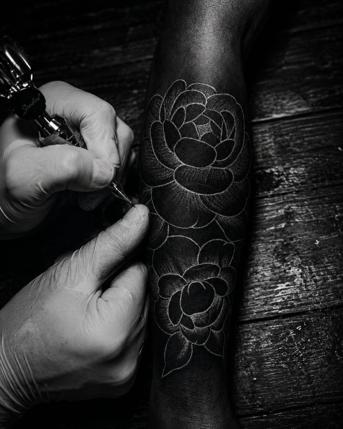 A tattoo artist inking blackwork florals onto a forearm